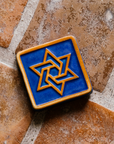 This square tile features a Star of David in its center with a simple line border around its edge.