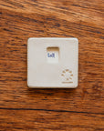 Back of a 3" x 3" tile with stamped-in notch for hanging. It is also stamped with the Pewabic logo, "Detroit", and specific Pewabic maker's mark.