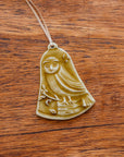 This bell-shaped ornament features a wide-eyed owl sitting on a fallen tree trunk, branches covered in leaves and berries surround it.
