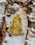 This bell-shaped ornament features a wide-eyed owl sitting on a fallen tree trunk, branches covered in leaves and berries surround it.