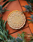 A Mooncake Paperweight in shimmering Blush Iridescent surrounded by thistle and wax flowers.