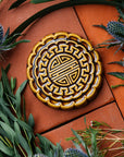 A Mooncake Paperweight in our glossy Molasses glaze, surrounded by thistle and wax flowers.