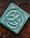 The Trinity Knot tile features a three-pointed Celtic knot interwoven with a circular ring. This knot is surrounded by a thick border with smaller three-pointed knots in each corner.