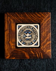A 4x4 Midnight Scraped University of Michigan Seal tile in a rich wood frame rests on a black surface
