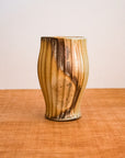 This Justin Lambert cup features a vase-like cup whose diameter starts smaller at the bottom, gets gradually wider then smaller again near the rim. There are vertical ridges and a moddled brown glaze.