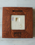 The back of the framed piece shows the open-back structure of the frame. This exposes the Pewabic Stamp one the back of the tile as well as the official sports licensing sticker. There is a burned on stamp of the woodworker who created the frame- it says "Handcrafted Family Woodworks".