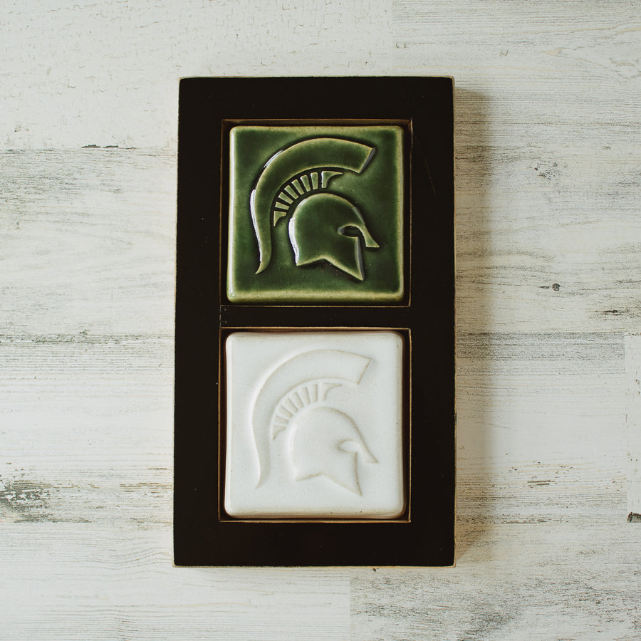 This black wooden framed piece features two Spartan tiles stacked on top of each other. Each tile has a high relief Spartan helmet design.. The top tile features the glossy deep green Kale glaze while the tile below has the satin finished white Alabaster glaze. 