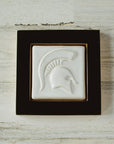 The Spartan Tile features a high relief design of a Spartan helmet with a large crest. This tile has the satin finished white Alabaster glaze and sits in a black painted wood frame.