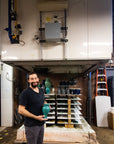 Kiln technician Brett holds a Large Classic Vase in Pewabic Blue glaze while standing in front of Pewabic's large Blaauw Kiln