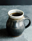 The Classic Mug is has rounded sides with a more narrow opening for drinking. The main body of the mug is the main glaze color while the inside and the lip are a coordinating color. This mug features the almost graphite looking black Carbon glaze with a gray lip.