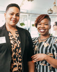 Two ladies smile and pose for a photo with black white and tan patterned attire