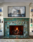 Vibrant, lit fireplace made up of Iridescent and matte glazes which creates an overall green, mirror-like effect. The white shelves on either side of the fireplace hold various ceramic pieces–– mostly in bright blue and ivory. There is a blue, gray, and white abstract painting above the mantel.