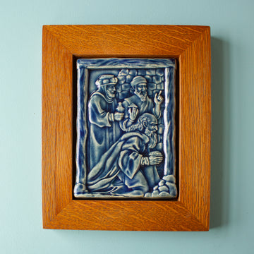 The Three Wise Men Tile features the wisemen in robes holding their three gifts- gold, frankincense and myrrh. They are all facing the right, they seem to be focused on one point. There is a stone wall behind them. This tile is in the glossy deep blue Ocean glaze which offsets the pale yellowish brown oak wood frame.