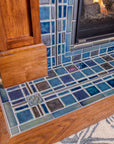 A detail shot of a fireplace and hearth made up of blue, gray, and charcoal tiles.