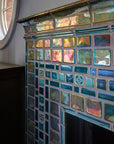 A corner detail shot of a neo-futuristic fireplace and hearth comprised of Iridescent tiles which are green/blue and mirror-like.