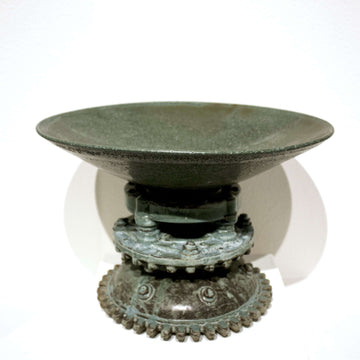 This shallow, wide bowl sits on a tall ornate stand made up of round gears and riveted domes all glazed in a patina of greens and grays.