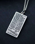 This brushed metal Detroit Map Pendant is rectangular with a line drawing of the areal view of a downtown Detroit street map. The word "Detroit" is written at the bottom of the design.