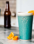 The Pewabic Pint is a simple ceramic pint glass with sides that slightly slope outwards to create a larger opening at the top. These pints feature smooth sides and have been stamped with the circular Pewabic logo on one side. The base color is featured on the sides of the cup with a coordinating color glaze inside that spills over about an inch onto the outer cup, with the two colored glazes meeting just above the logo. This Pint features the matte turquoise Pewabic Blue glaze with a white interior and lip.
