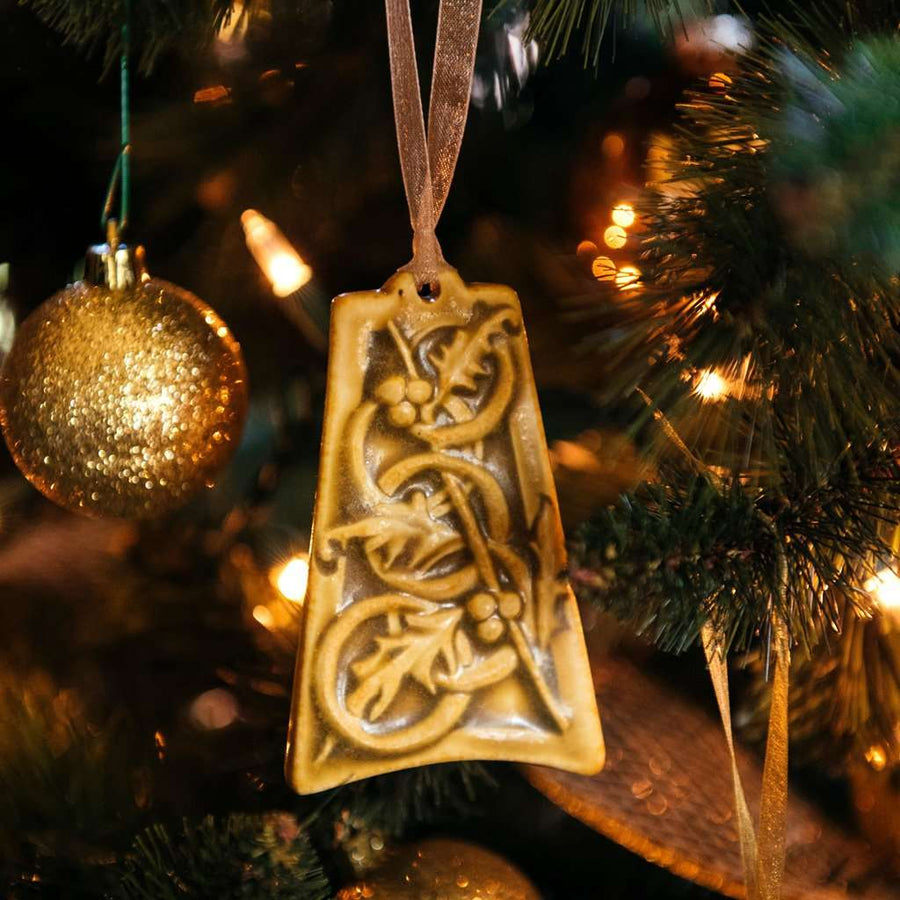 The ceramic Five Gold Rings Ornament hangs on a lighted Christmas tree with gold sparkling decorations.
