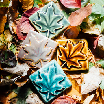 All four colors of the maple leaf embossed tile are resting on a bed of fall leaves. Each maple leaf design covers the entire surface of the tile. 