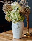 A Birch Pinecone vase holds a large bouquet of bushy hydrangeas.