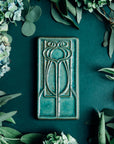 This vertical rectangle tile has an abstract low relief design. Interconnecting hard and curved lines come together to create a craftsman style motif.