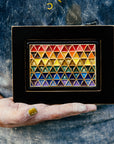A Pewabic Artisan holds the framed Pride Tile in their dusty hands against their well-worn apron.