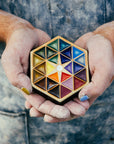 A Pewabic employee wearing a well-used denim apron holds the colorful Hex Paperweight in their dust-covered hands.