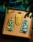 Three ceramic ornaments are sitting in a gift box and placed under a Christmas tree.