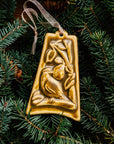 The bell-shaped Partridge in a Pear Tree Ornament features a partridge sitting on the branches of a tree with one large pear dangling from its branches. The ornament is glazed in a creamy brown color.