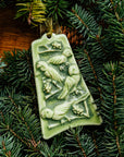 The bell-shaped Four Calling Birds Ornament features four parrots siting on the branches of a berry-covered tree. The ornament is glazed in a matte green color.