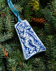 The bell-shaped Eleven Pipers Piping ornament features a man wearing a medieval costume with a feather in his hat. He is playing a long conical pipe and there are eleven musical notes surrounding him. The ornament is glazed in a matte blue glaze.