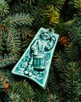 The bell-shaped Twelve Drummers Drumming Ornament features a man wearing a Revolutionary War era uniform, buckled boots and a three-cornered hat. He is standing at attention with his arm raised to hit the drum attached to his body by a strap over his chest. There are twelve stars in the air around him.