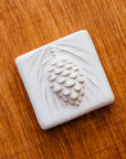 The ceramic Pinecone Tile has a high relief design with one large pinecone in the center and long spindly pine needles framing it.