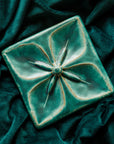Geo Flower Tile in our classic Pewabic Blue glaze nestled in a rich, green velvet fabric.