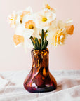 The Snowdrop vase has a wide, round base that contracts into a pillar as it gets taller. The rim of the vase has small snowdrop flowers whose stems glide gracefully down the sides of the vase.