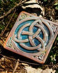 The Trinity Knot tile features a three-pointed Celtic knot interwoven with a circular ring. This knot is surrounded by a thick border with smaller three-pointed knots in each corner.