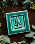 The Pine Tree Tile features a 3D outline of a pine tree inside of a thick, smooth square border. This tile features the matte turquoise Pewabic Blue glaze.