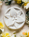 This circular tile has a high relief trillium flower centered within the design. It petals stretch out to the very edges of the circle and overlap the tile's simple line border.