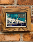 The framed Belle Isle Tile hangs on a red brick wall.