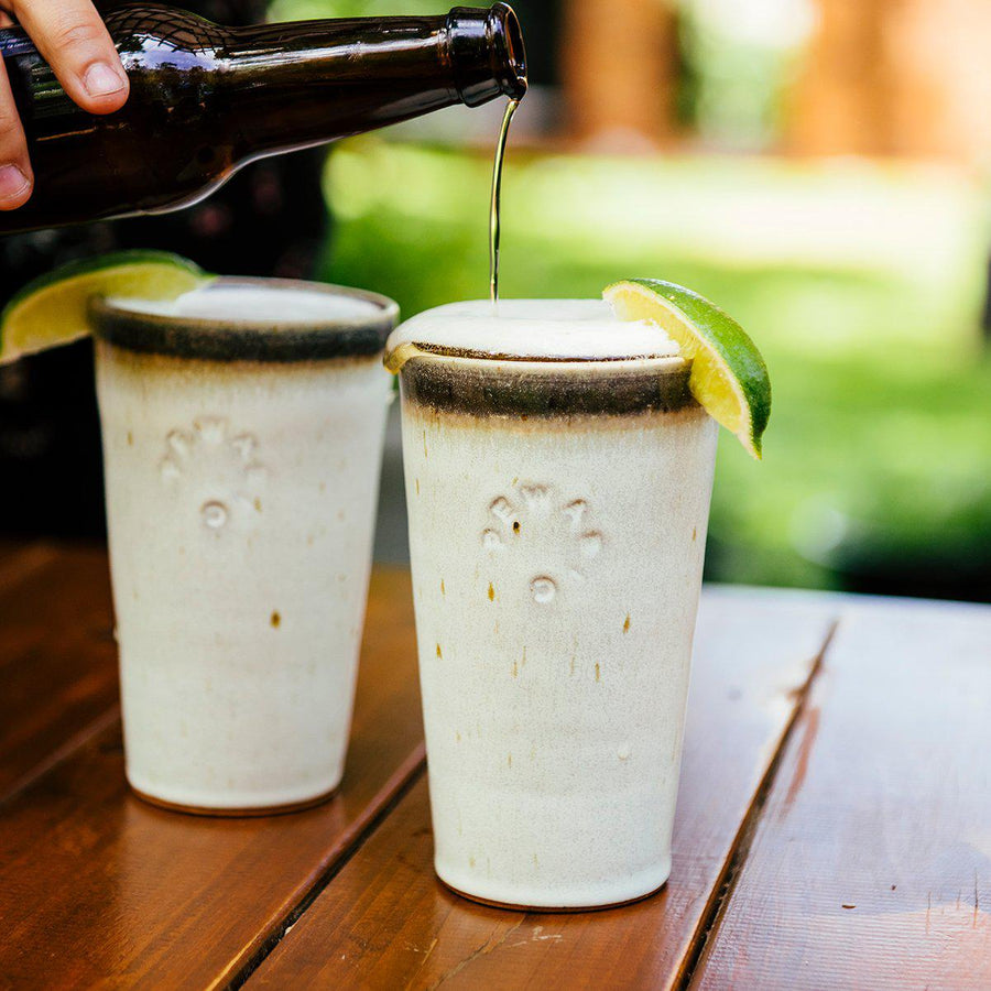 Two Birch Pints sit on a picnic table, each is filled to the brim with frothy beer and a slice of lime. The Birch glaze meets the gray glaze and somehow create an earthy brown that connects the two.