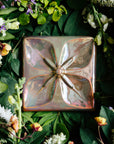 The Flower Geo Tile features a four-petaled flower. Each petal takes up a quarter of the tile, making a perfectly geometric shape. The inner part of the flower is round with four cattail shaped stamen exploding from the center that point out to the corners of the tile.