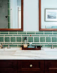 The green Pewabic tiles on the bathroom walls are like a thick border behind the double sink with white marble countertops.
