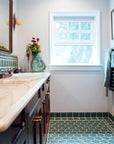 Bright white walls and a large window showcase the soft green of the tile. While the dark wood cabinets and mirror frames give a cozy look.