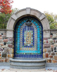 Square tiles in multiple shades of blue are positioned in different designs throughout this flat tile installation. It it tucked into an alcove on a stone wall.