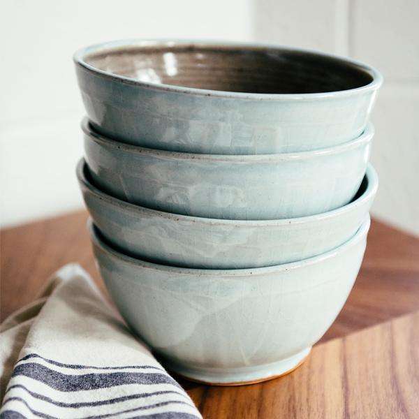 A stack of Frost glazed bowls sit on a wooden countertop.