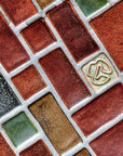 1:1 aspect ratio close-up shot of the red, tan, pine green, charcoal, and "blush" iridescent tiles in this autumnal design.