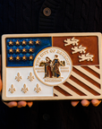 A person in a dark, navy, knit sweater is holding our new hand-painted Detroit Flag Tile.