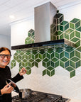 A quarter angle shot of the custom Green Rhombus Backsplash. There is a woman wearing glasses smiling as she opens the lid of a pot placed on the stove.