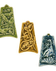 Three colorfully embossed ornaments are against a white background: one has four parrots resting tree branches covered with berries, another has five intertwined rings with holly and berries strewn around them, the last has a goose keeping watch over her nest filled with six eggs.